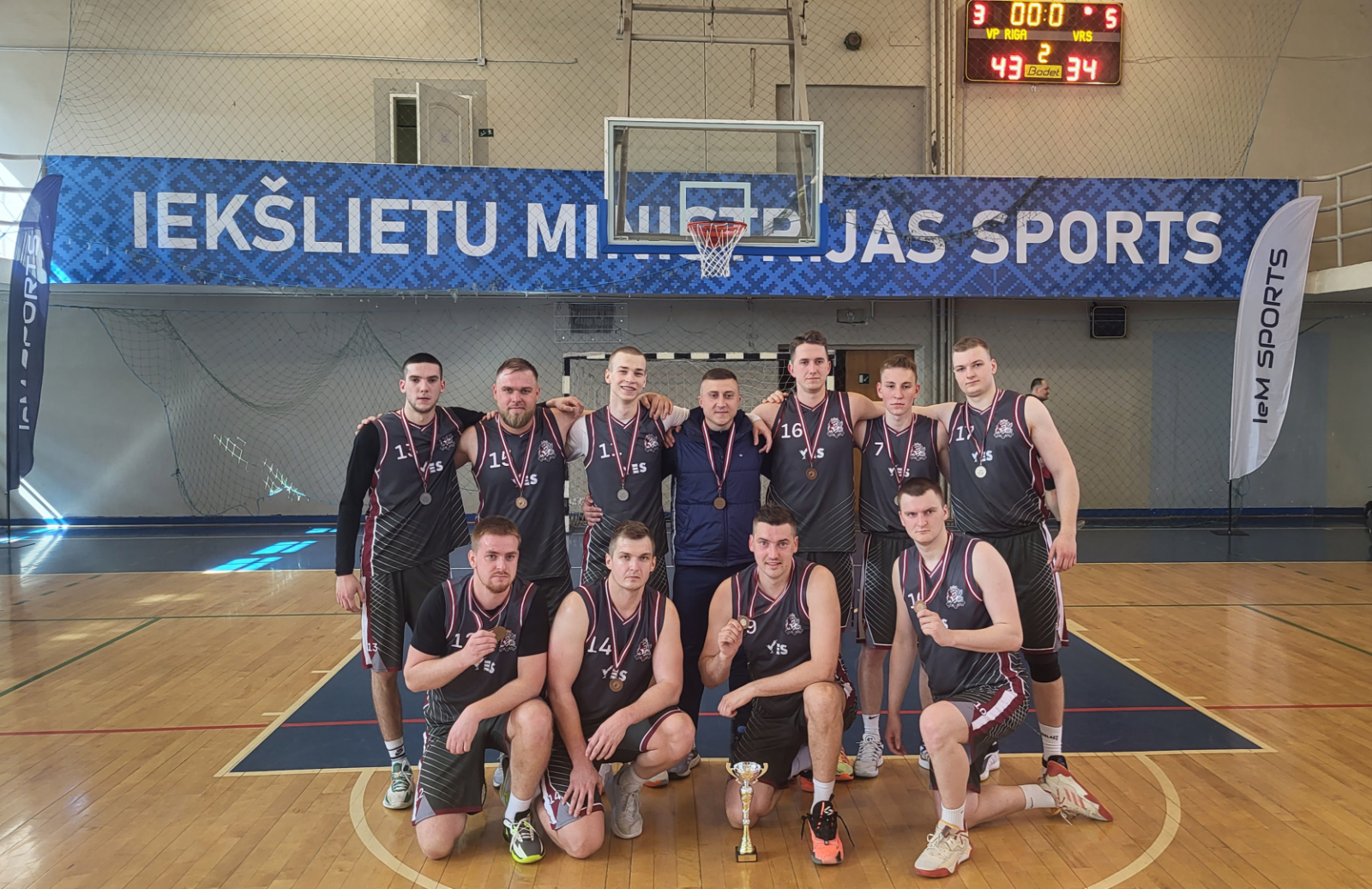 Basketbola sacensību trešās vietas ieguvēji – Valsts robežsardzes komanda sporta zālē, priekšā uz grīdas kauss, spēlētājiem kaklā bronzas medaļas