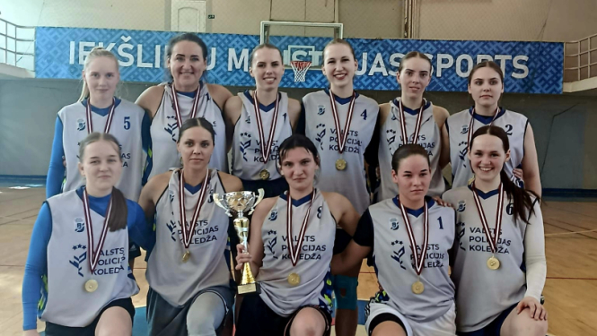 Basketbola sacensību čempiones – Valsts policijas koledžas komanda sporta zālē, visām spēlētājām kaklā zelta medaļas, vienai spēlētājai – komandas izcīnītais kauss.