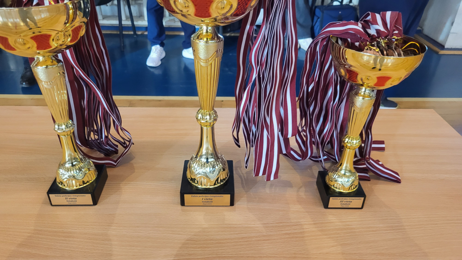 Trīs metāla kausi zelta krāsā laureātu apbalvošanai kausos medaļas ar lentēm Latvijas karoga krāsās