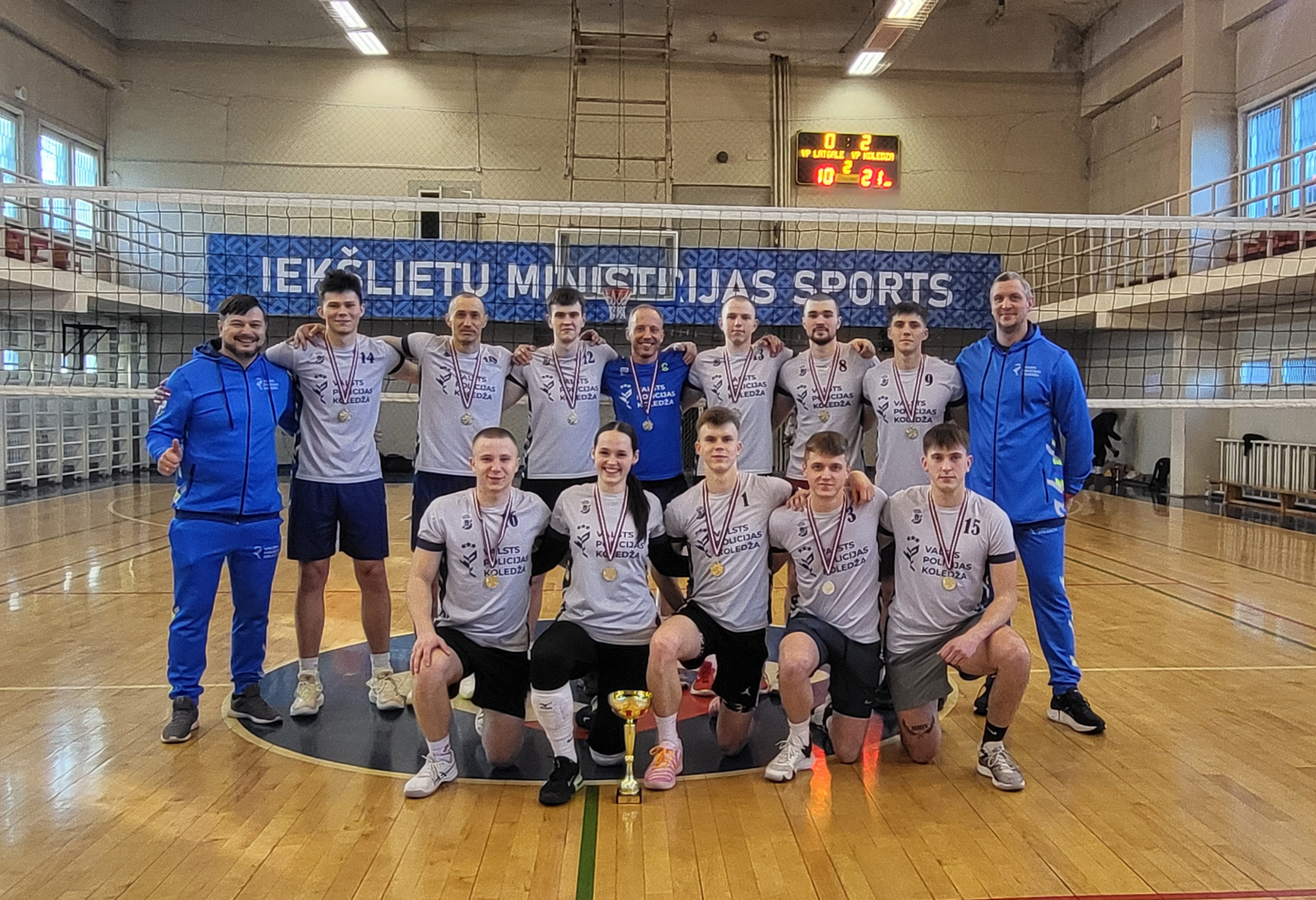 Volejbola sacensību čempioni pirmās vietas ieguvēji Valsts policijas koledžas komandas spēlētāji ar medaļām kauss priekšā uz grīdas Kopā ar komandu Valsts policijas koledžas direktors Dmitrijs Homenko un Sporta katedras vadītājs Oskars Vaisjūns