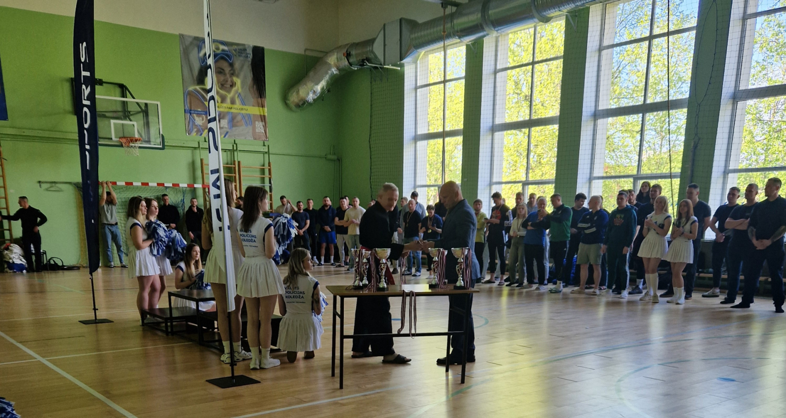 Mirklis pirms apbalvošanas. Vsevolods Zeļonijs spiež roku Robertam Hvesko, blakus pjedestālam stāv karsējmeitenes. Sacensību uzvarētāji gaida izcīnīto balvu pasniegšanu.