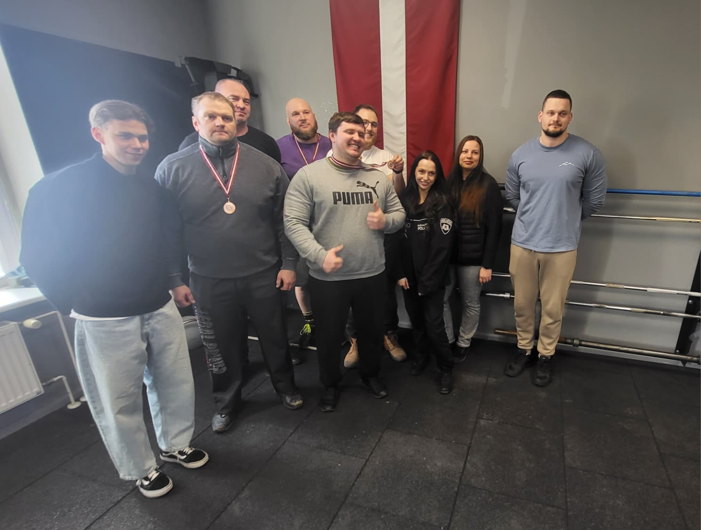 Rīgas valstspilsētas pašvaldības policijas komanda, 9 cilvēki, 2 sievietes, 7 vīrieši, trim no viņiem kaklā medaļas, fonā Latvijas karogs