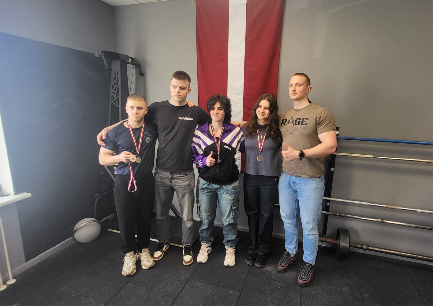 Valsts policijas koledžas komanda, 5 cilvēki, divas sievietes, abām sievietēm kaklā medaļas, trīs vīrieši, vienam no vīriešiem viena medaļa pakārta kaklā, otra ir rokā, fonā Latvijas karogs