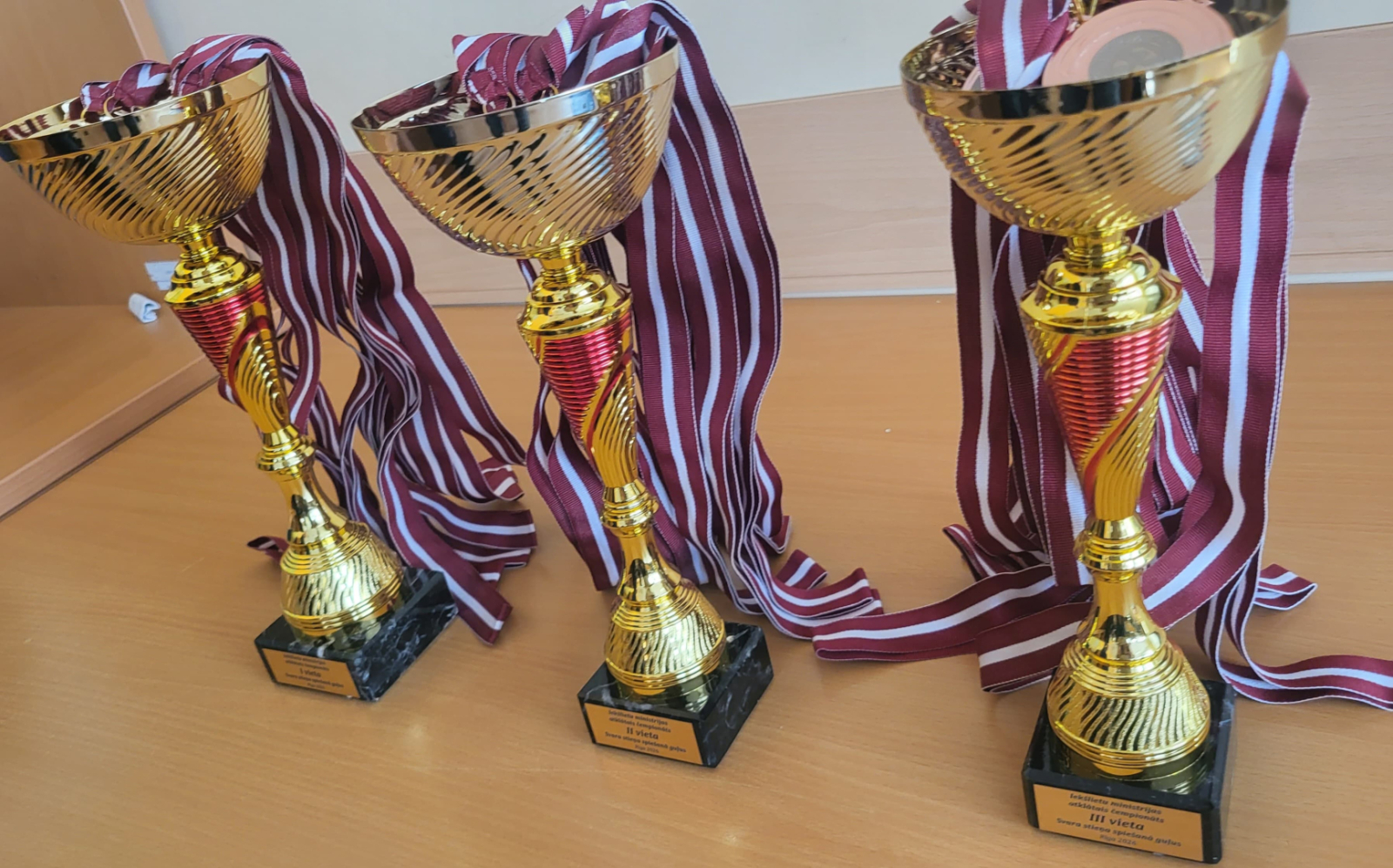 Trīs kausi sacensību uzvarētāju apbalvošanai. Kausos atrodas medaļas ar lentēm Latvijas karoga krāsās