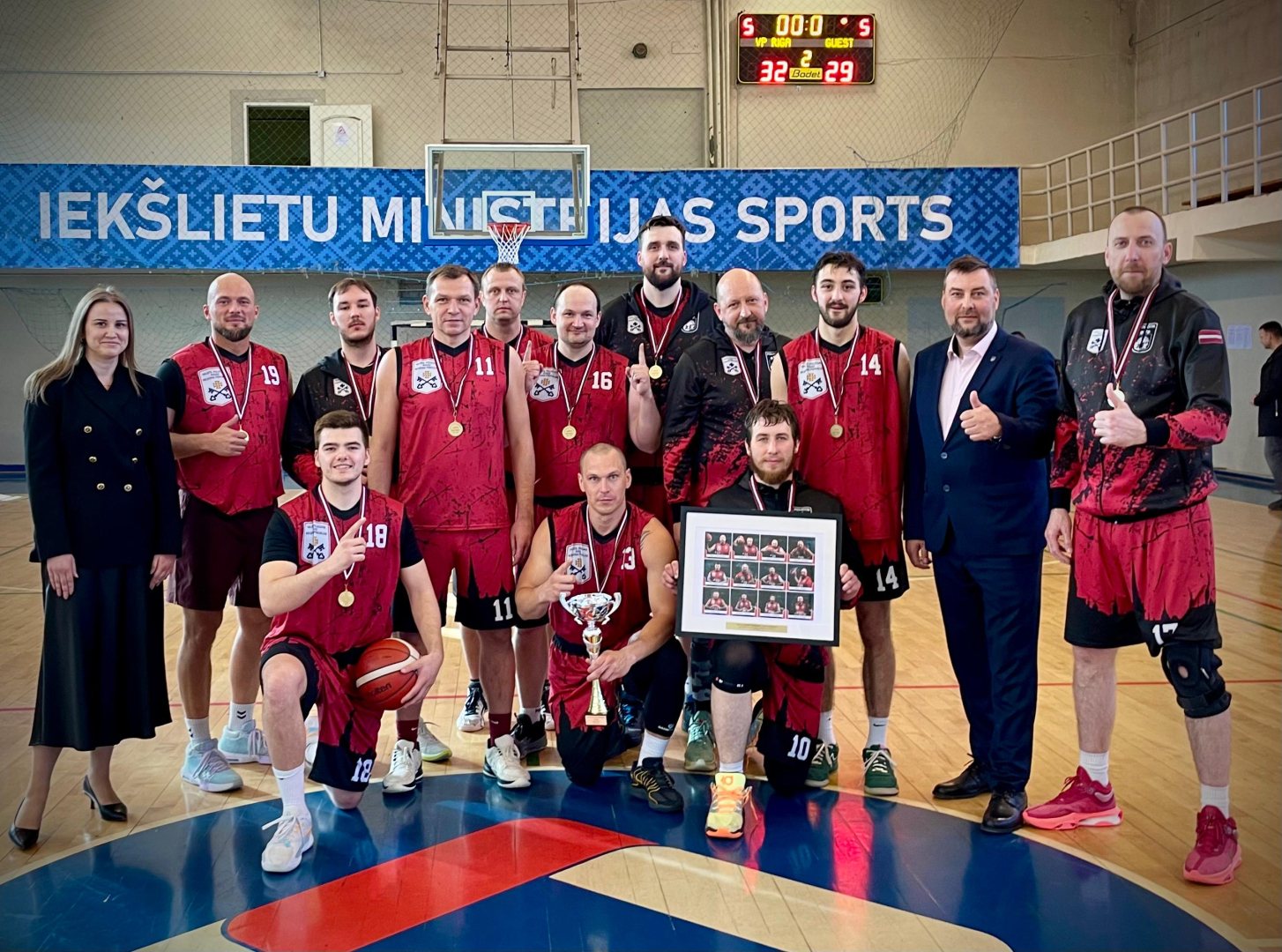 Valsts policijas čempionāta sacensību basketbolā uzvarētāju kopbilde sporta zālē. Fonā baneris ar uzrakstu Iekšlietu ministrijas sports.